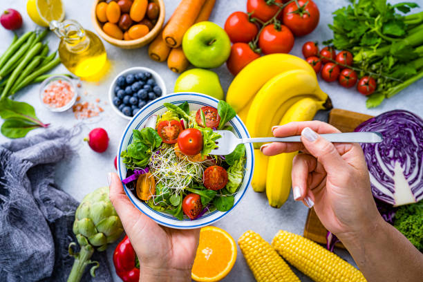 Hands holding healthy salad surrounded by fresh vegetables and fruits